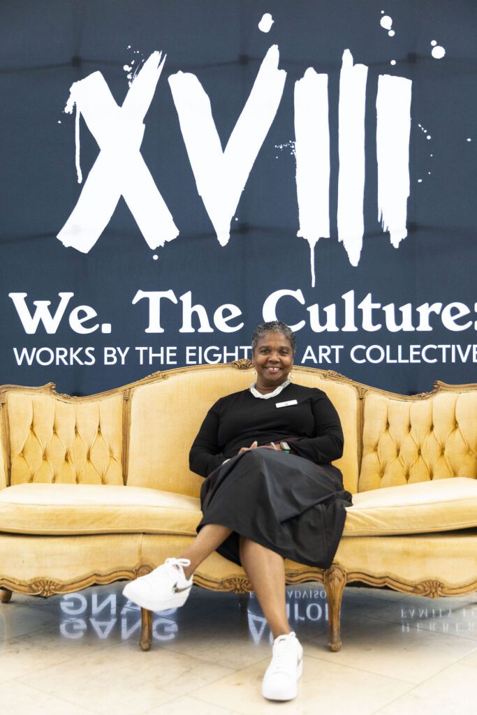 Newfields CEO and President Colette Pierce Burnette poses on a couch in front of the "We. The Culture" exhibition at Newfields.