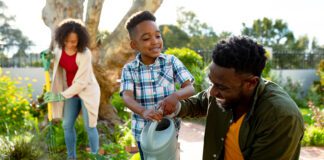Happy african american father and son watering plants together. family time, having fun together at home and garden.
