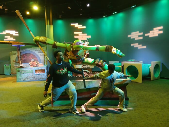 Just inside the exhibit are statues of each Teenage Mutant Ninja Turtle. Djibril, 17, and Adama, 12, visited the exhibit with Recorder Production Manager Jeana Ouattara during its opening March 9. (Photo/provided)