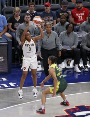 WNBA player shoots a three-pointer over another player.