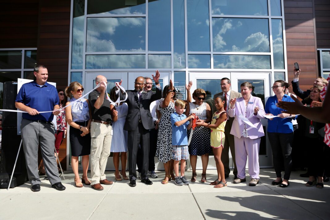 Students, teachers, and administrators cut a ribbon in front of a new elementary school