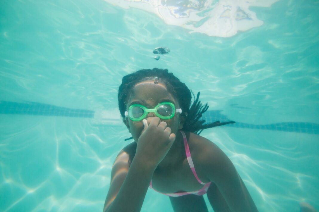 Young girl swims underwater while holding her nose and wearing goggles