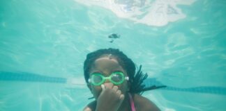 Young girl swims underwater while holding her nose and wearing goggles