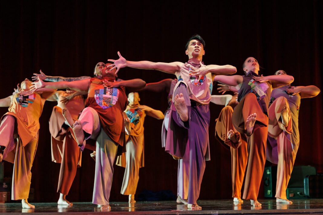 A group of dancers strike a collective pose with open arms and one leg raised