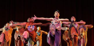 A group of dancers strike a collective pose with open arms and one leg raised