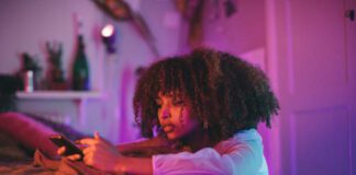 A girl looks sadly at her phone in her bedroom under pink lights