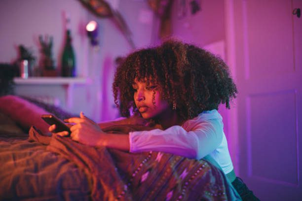 A girl looks sadly at her phone in her bedroom under pink lights