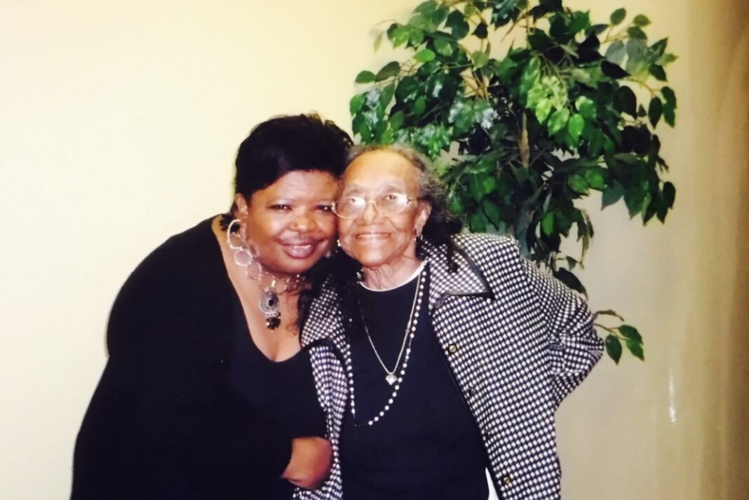 A woman poses with an older woman beside a tree.