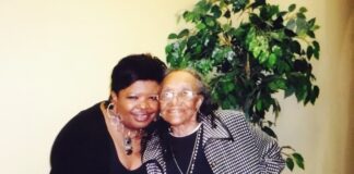 A woman poses with an older woman beside a tree.