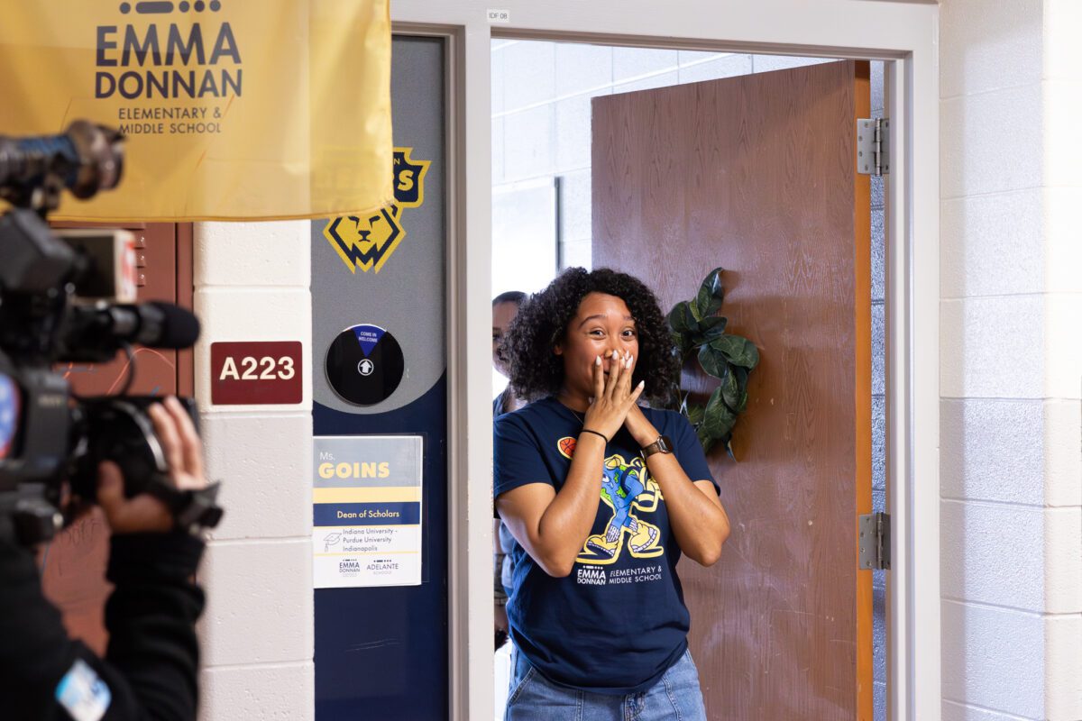 A woman stands with her hands over her face in surprise as she enters a classroom