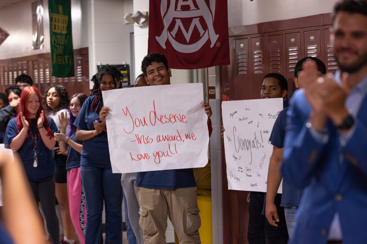 students stand with signs congratulating their teachers 