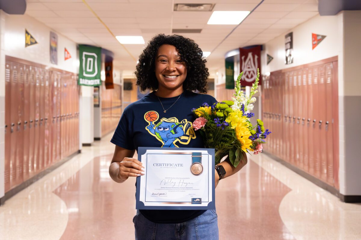 A woman holds a certificate and flowers in a hallway