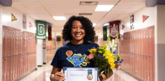 A woman holds a certificate and flowers in a hallway