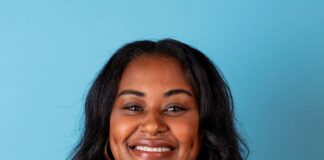 Black woman with dark hair and dark clothing smiles with a blue backround