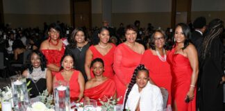 Several women dressed in red pose at a banquet table at a gala