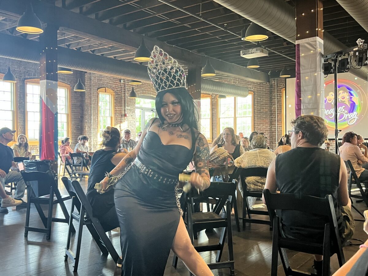 A person in a crown and black dress poses with one leg out .