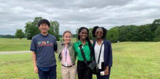 four kids stand together in navy blue, white and light pink on a grassy knoll, with dark green in the background