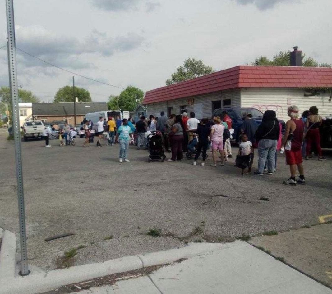 people are lined up at a vacant lot beside a white building with a red roof