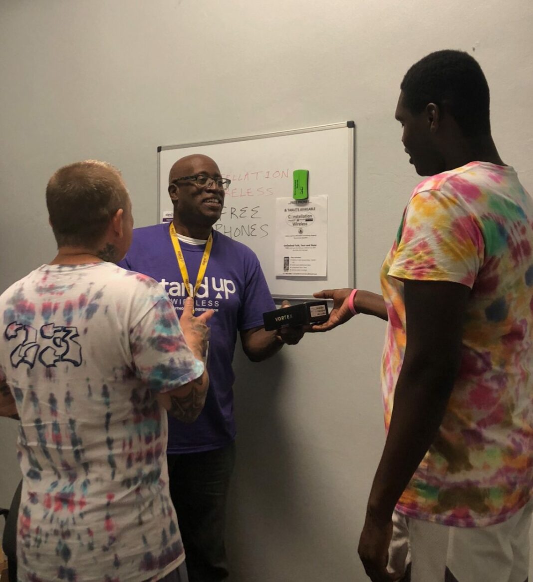 a man in a purple shirt hand phones to two men in tie dye shirts