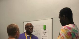 a man in a purple shirt hand phones to two men in tie dye shirts