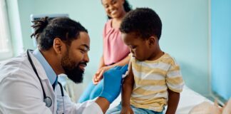 Young African American doctor gives immunization to small African American boy in doctor's office while his mother watches
