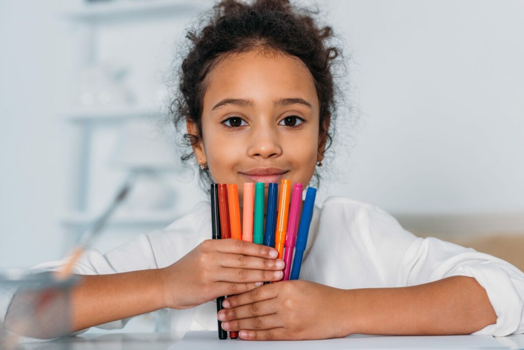 adorable african american kid holding colored felt pens and looking at camera at home