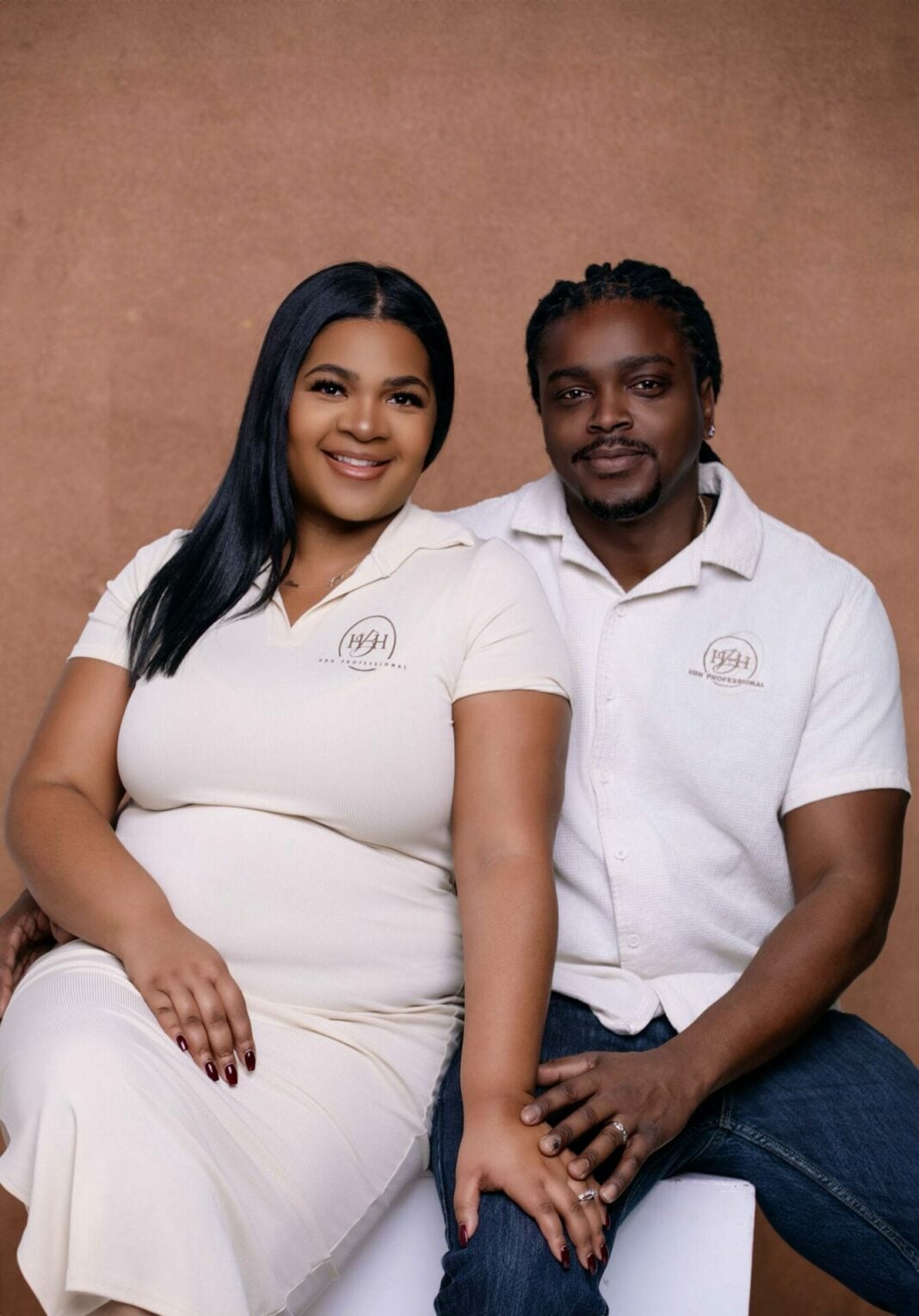 a husband and wife in white pose in front of a brown background