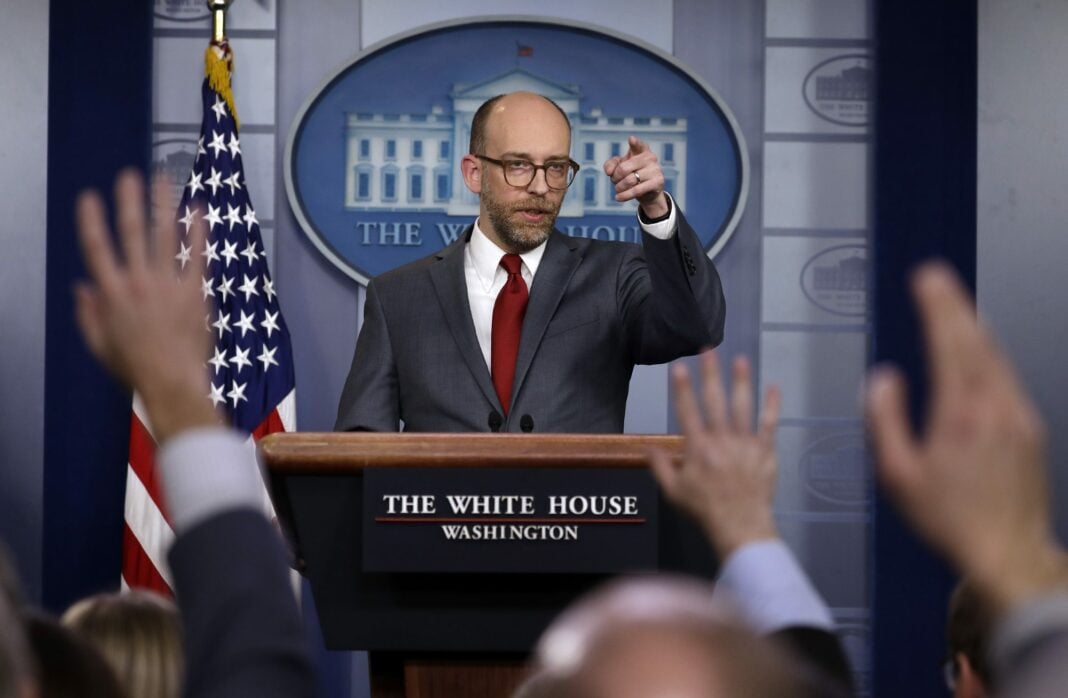 man speaks at podium in front of press at White House