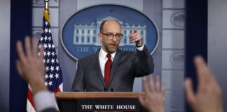 man speaks at podium in front of press at White House