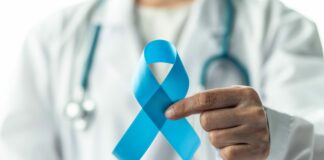 doctor in white coat holds up blue ribbon for prostate cancer awareness