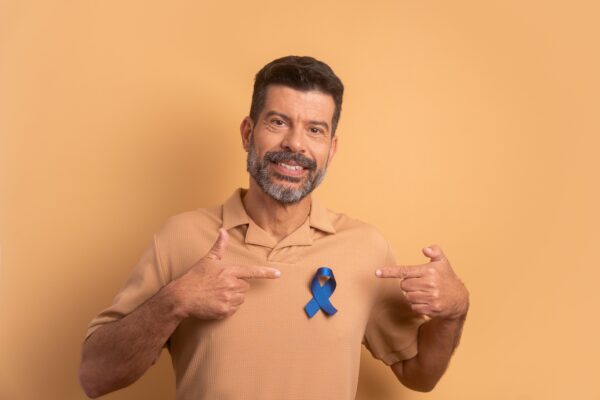 man in beige shirt points to blue ribbon for prostate cancer awareness month