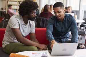 Male University Student Working In Library With Tutor