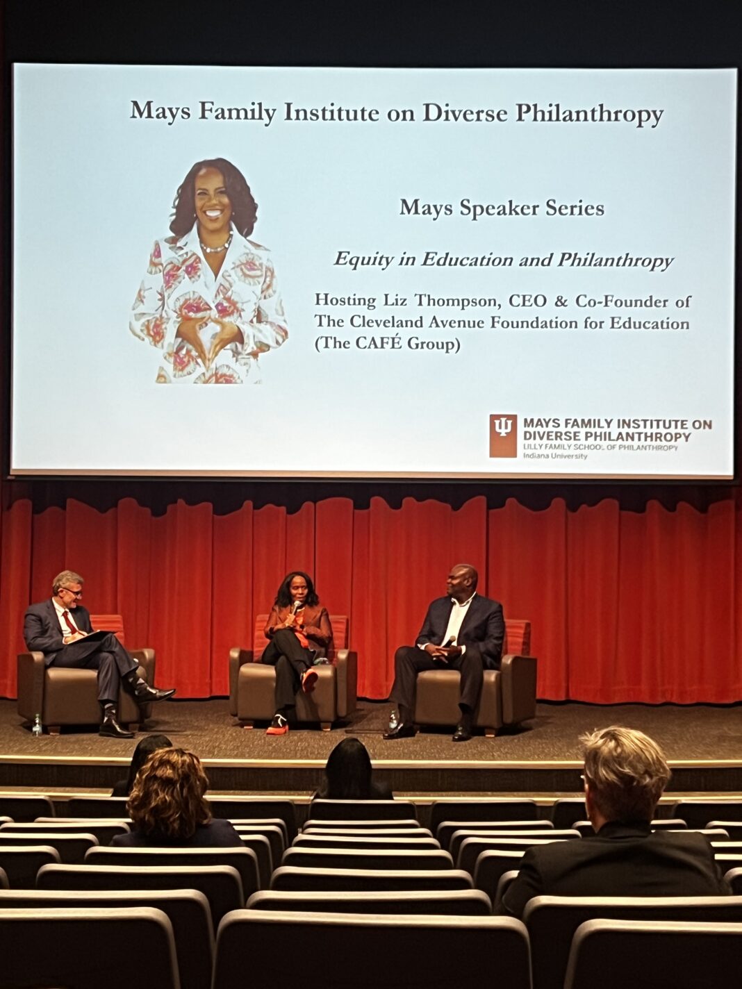 woman and two men sit against red background to discuss their work on a panel