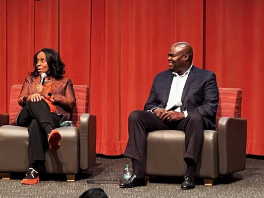 Liz and Don Thompson sit aginst red background speaking about the cafe group
