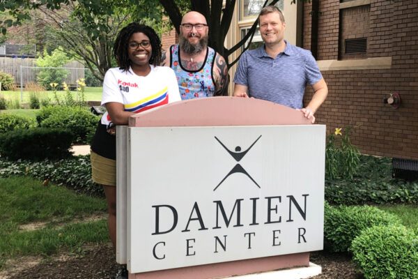 three people pose in front of damien center