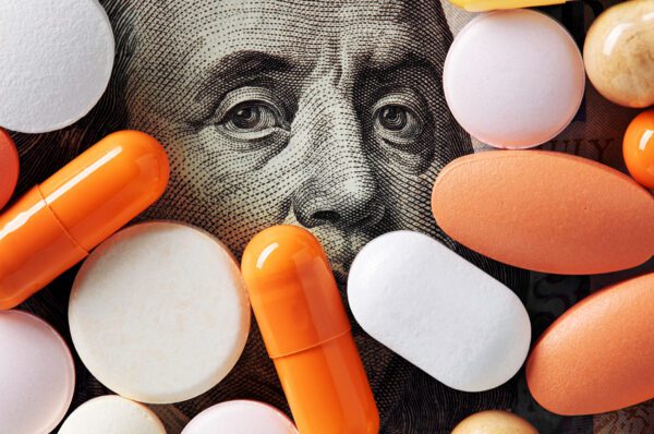 Capitalism and healthcare policy concept. Colorful medical pills cover Benjamin Franklin's face on one hundred american dollar bill. Macro top down view.