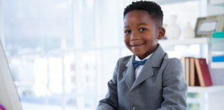 Portrait of boy imitating as businessman using computer at desk in office