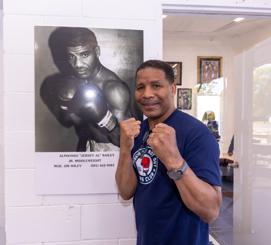 Boxer Alphonso Bailey posing in front of a photo of himself at his Down But Not Boxing gym in 2025.