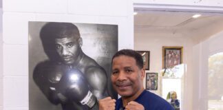 Boxer Alphonso Bailey posing in front of a photo of himself at his Down But Not Boxing gym in 2025.