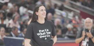 WNBA CBA Caitlin Clark wearing Pay Us What You Owe Us protest shirt during WNBA All Star in Indianapolis in July of 2025.