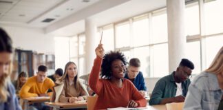 Happy African American student raising her hand to ask a question during lecture in the classroom.