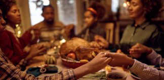 Close of kids saying grace while having Thanksgiving dinner with their family at dining table. (Photo/Getty Images)