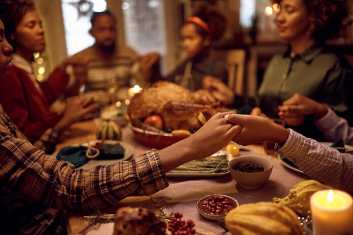Close of kids saying grace while having Thanksgiving dinner with their family at dining table. (Photo/Getty Images)