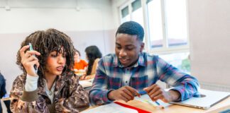 Two high school students are working together on a project, sharing ideas and discussing the task at hand in a classroom setting