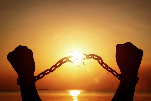 Silhouette of raised hands breaking chains on sunset background. Concept of fight for freedom, and overcoming limitations.