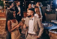 Beautiful young African couple in formalwear holding champagne flutes and smiling while spending time with friends on night party. (Photo/Getty Images)