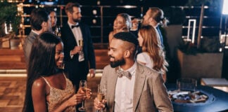 Beautiful young African couple in formalwear holding champagne flutes and smiling while spending time with friends on night party. (Photo/Getty Images)