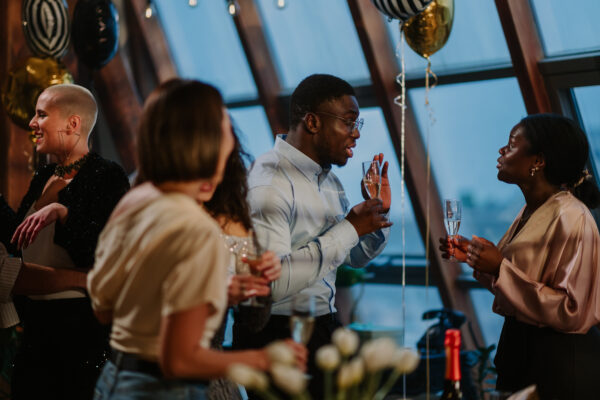 Diverse friends socializing at a rooftop party, enjoying a celebratory event with champagne glasses and balloons. (Photo/Getty Images)