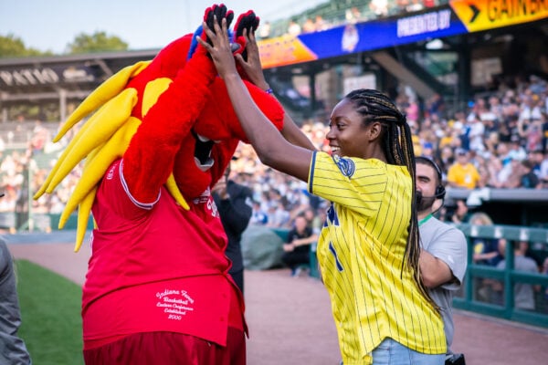 Simone Biles Owens playfully interacts with the Indiana Fever mascot, Freddy Fever, near the dugout area. (Photo/Josh Herd)