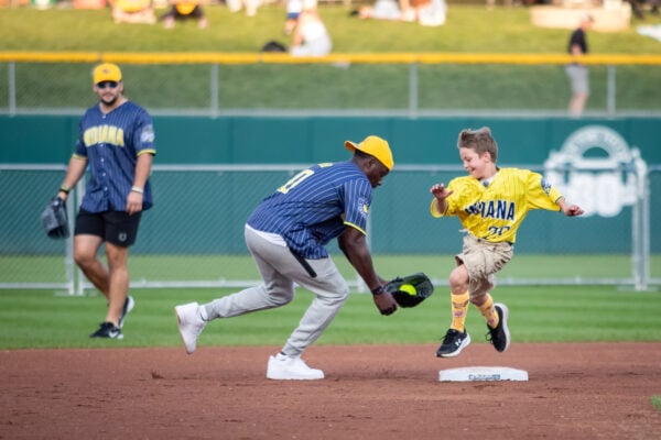 A young fan leaps onto a base with a huge smile as a player in a blue pinstripe jersey playfully fields the ball near him. (Photo/Josh Herd)